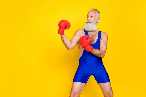 Side profile photo of old aged pensioner professional fighter boxing gloves serious look empty space stadium advert grimace isolated on yellow color background.