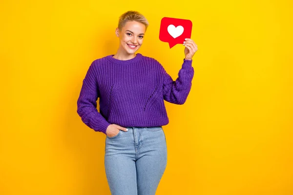 Portrait of good mood woman with short hair violet sweater hold red paper heart hand in pocket isolated on yellow color background.