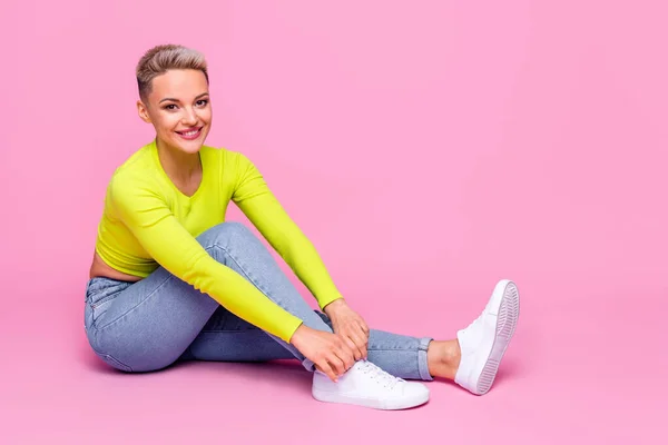 Full body profile photo of positive cute lady sit floor tying shoe laces isolated on pink color background.