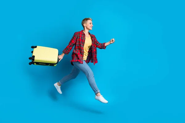 Full length size photo of young excited funny woman running fast hurry airport destination excursion hold suitcase isolated on blue color background.