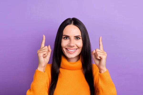 Photo positive young charming lady wear stylish orange turtleneck direct fingers up empty space recommend product isolated on violet color background.