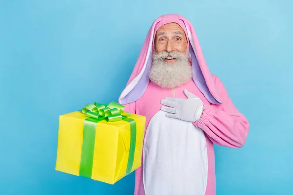 退休人士喜形于色 身穿粉红兔子服装 手持棕榈放在蓝色背景的黄色礼品盒上的照片 — 图库照片