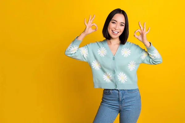 Photo of optimistic pretty japanese girl wear blue daisy ornament jumper show okay sign approve quality product isolated in yellow color background.
