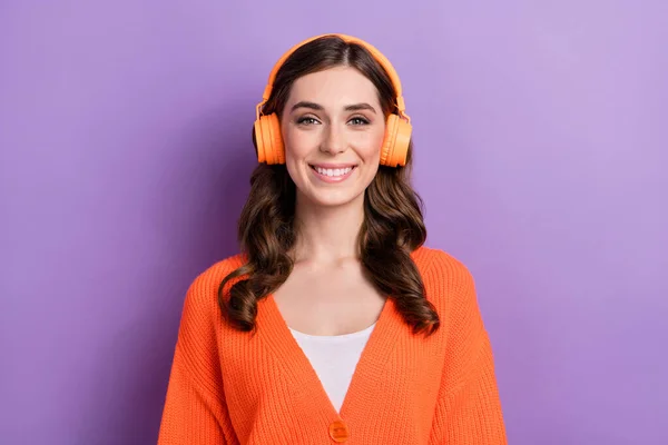 年轻而积极的女士穿着橙色羊毛衫欣赏音乐的肖像照片 她的新无线耳机被紫色背景隔离了 — 图库照片
