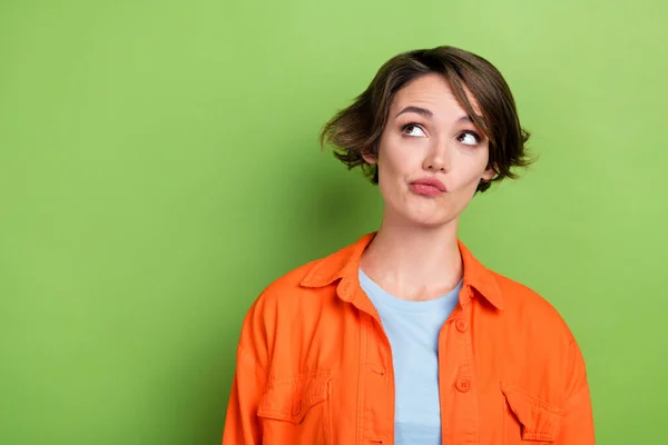 Photo of pretty lovely minded lady wear bright orange trendy clothes suspiciously look empty space isolated on green color background.