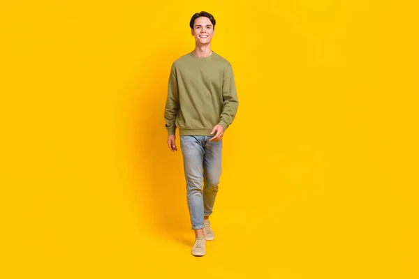 Full body photo of satisfied positive man toothy smile walking empty space isolated on yellow color background.