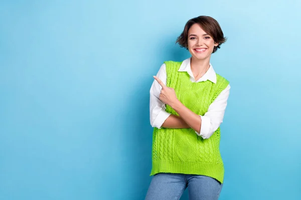 Photo of young optimistic attractive business lady wear knit green vest indicate finger empty space it school promo isolated on blue color background.