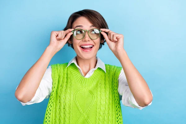 Photo of young excited lady librarian wear green vest try new glasses checkup lenses look empty space letters isolated on blue color background.
