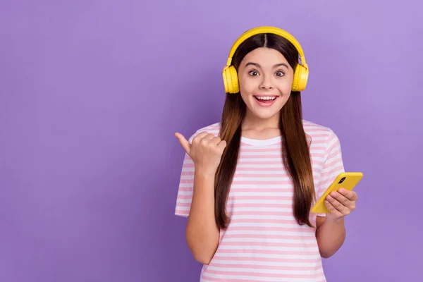 Photo of adorable excited lady wear striped t-shirt listening music modern device thumb empty space isolated violet color background.