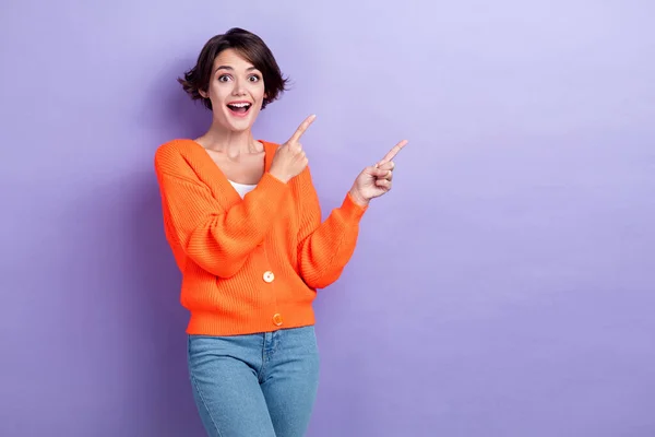 Photo of cheerful excited lady dressed orange cardigan open mouth pointing two fingers empty space isolated purple color background.