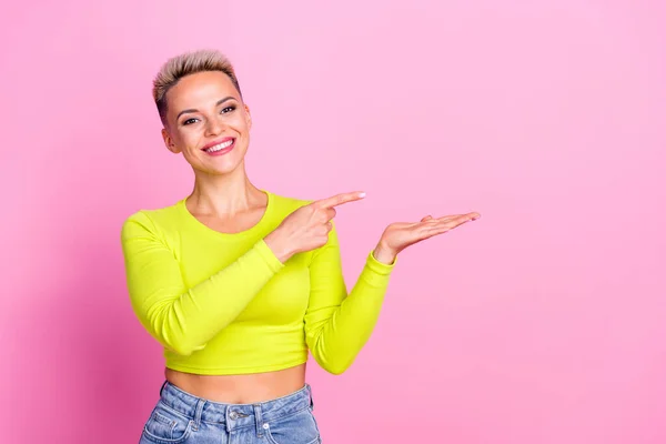 Photo of gorgeous cheerful girl toothy smile direct finger arm hold empty space isolated on pink color background.