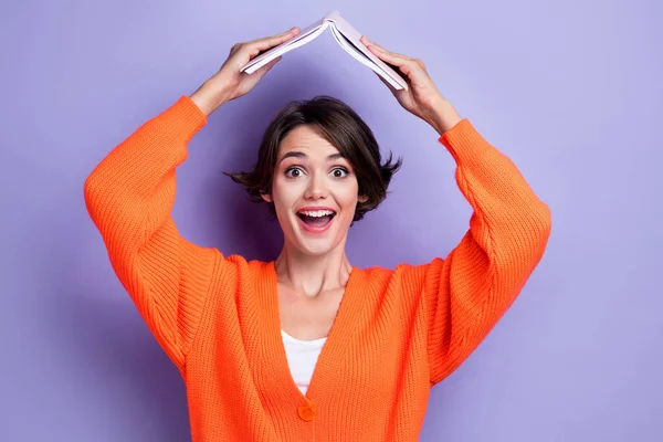 Photo of cheerful glad excited lady wear stylish clothes hand hold book above head good mood isolated on purple color background.