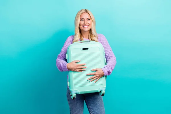 Portrait of nice satisfied person arms hold suitcase toothy smile isolated on turquoise color background.