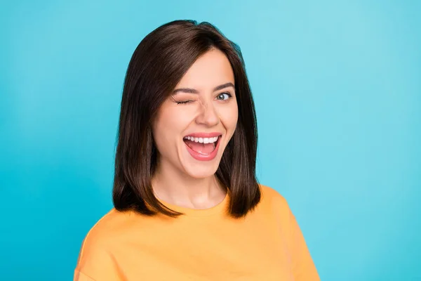 Portrait of funny satisfied pretty naughty woman with long hairstyle dressed yellow t-shirt blinking eye isolated on blue color background.