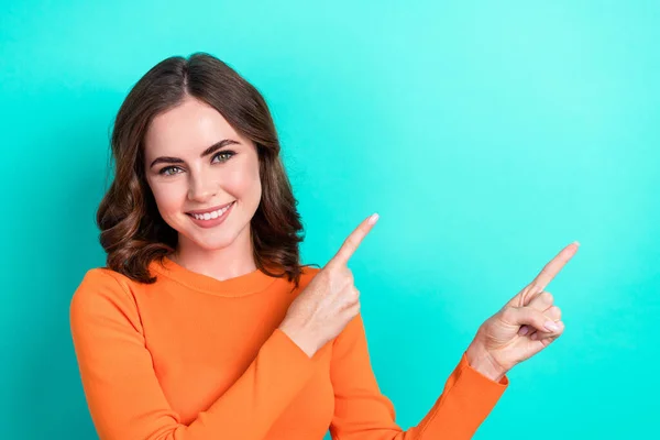 Photo of young cheerful positive woman wear orange top smile direct fingers empty space recommend new salon ad isolated on cyan color background.