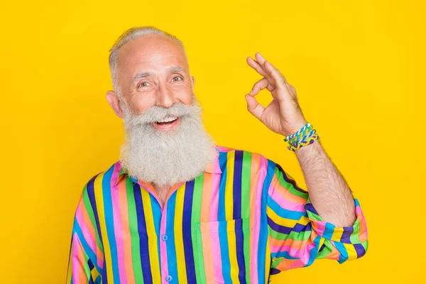 Photo of cheerful optimistic satisfied man with white beard dressed striped shirt showing okey isolated on yellow color background.