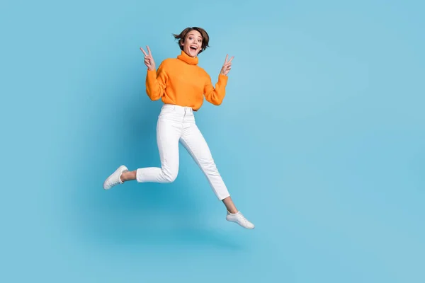 フル長さ写真の美しい若い女性ジャンプショーダブルVサインアクティブ摩耗トレンディーなオレンジ色の衣装に隔離された青の色の背景 — ストック写真