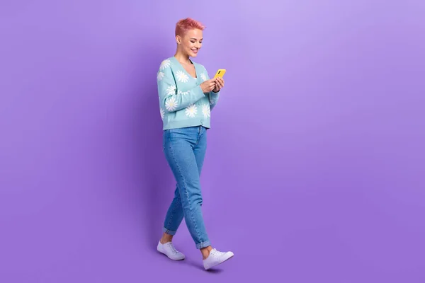 正の若いファンキーな女の子のフルボディ長幹部は 青スタイリッシュなプルオーバーを身に着けていますスマートフォンのブラウズは 紫の色の背景に隔離された — ストック写真