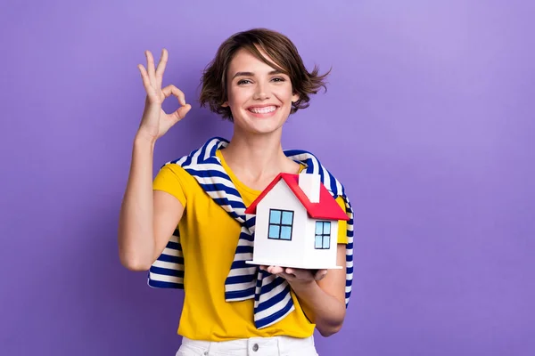 迷人的积极女士穿着时髦条纹衣服的照片拿着迷你房子的标志漂亮的购买隔离紫色背景 — 图库照片