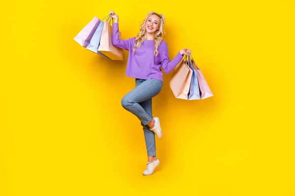 フルサイズの写真のかなり若い女の子保持ショッピングバッグパッケージ服スタイリッシュなバイオレット服孤立した黄色の色の背景 — ストック写真