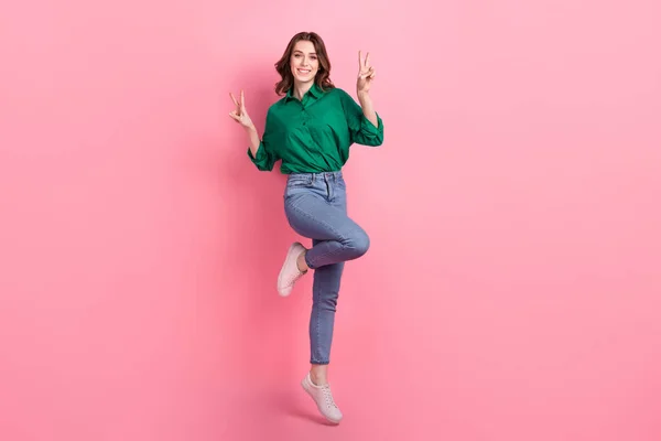フルサイズ写真の陽気面白いです可愛いです楽観的な女の子身に着けているジーンズ緑のシャツショーVサインジャンプ孤立したピンクの背景 — ストック写真