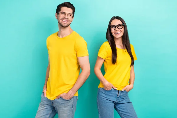 Photo of two teammates partners yellow t-shirts denim jeans hands pockets stylish ray ban glasses good job isolated on aquamarine color background.