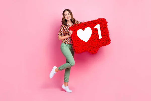 Full length photo of hipster girl hold big paper like symbol share repost youtube channel blogger enjoy her job isolated on pink color background.