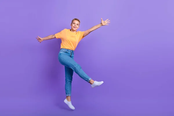 楽しいフレンドリーな女の子のジーンズの完全な長さの写真白いスニーカー飛んで楽しいを持っている分離された紫色の背景 — ストック写真