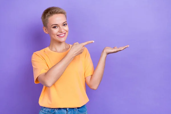 快乐乐观的年轻满意的促销小姐身穿橙色T恤 手握手掌 直接用手指把紫色背景隔离起来的照片 — 图库照片