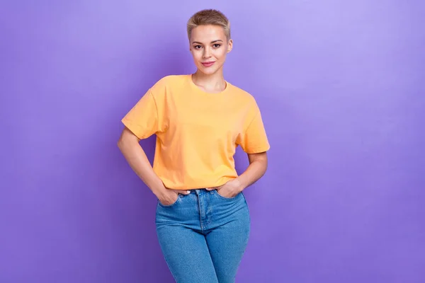 若い愛らしい自信の女性の写真は デニムジーンズの手のポケットオレンジTシャツポーズモデル広告バナー紫色の色の背景に隔離された — ストック写真