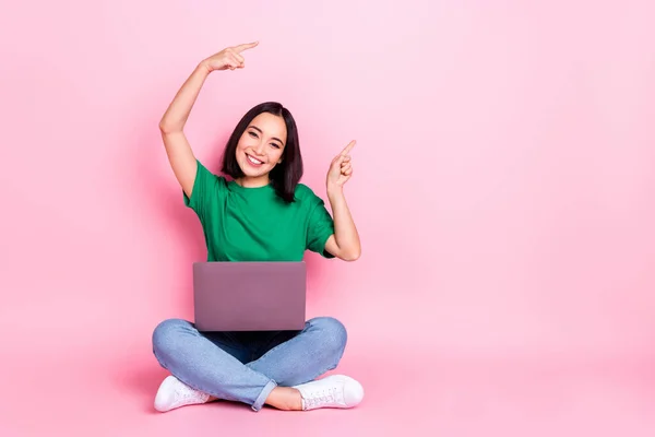 Full size photo of cheerful woman wear oversize t-shirt sitting with laptop indicating empty space isolated on pink color background.