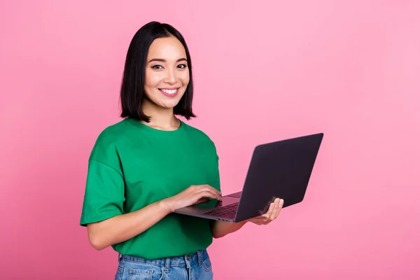 照片上 一个穿着绿色T恤衫 头戴短发 积极可爱的女孩 带着笔记本电脑在线购物 背景是粉色的 — 图库照片