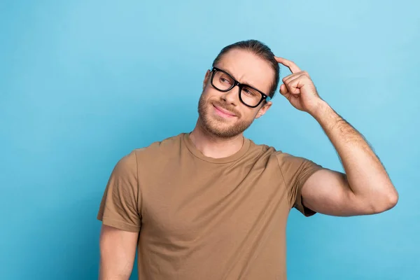 Photo of good mood smart guy with tail hairdo dressed beige t-shirt thoughtfully look empty space isolated on blue color background.