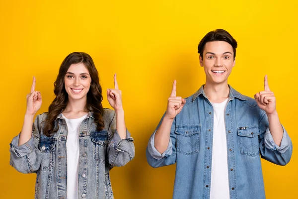 Photo of two cheerful funny people toothy smile direct fingers up empty space isolated on yellow color background.