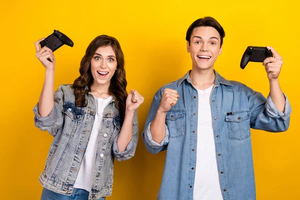 stock image Photo of two astonished positive partners hold gamepad raise fist achievement isolated on yellow color background.