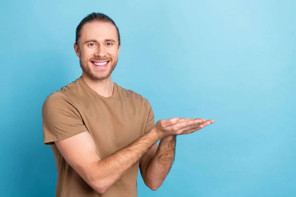 Photo of cheerful pretty man wear beige t-shirt smiling holding arms empty space isolated blue color background.