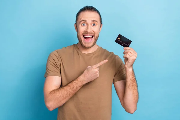 Photo of entrepreneur man wear t-shirt direct finger surprised demonstrate plastic credit card wireless nfc payment isolated on blue color background.
