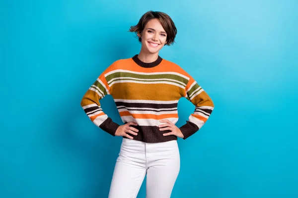 Photo of cheerful charming lady wear striped sweater hands arms waist smiling isolated blue color background.