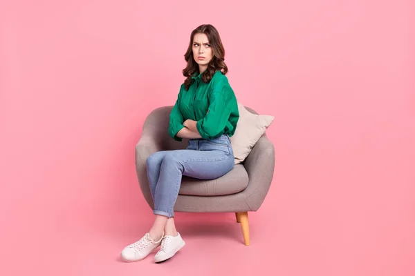 stock image Full size photo of offended unhappy girl dressed green shirt sit on armchair.offendedly look at empty space isolated on pink background.