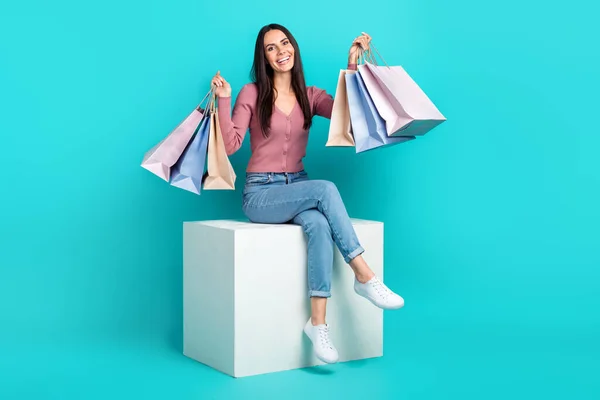 Full body cadre of sit white platform girl raise hands up hold much packages with brand clothes shopaholic isolated on aquamarine color background.