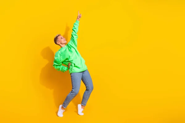 Full body length photo of hipster dancer lady wearing modern trendy outfit finger point up look empty space club isolated on yellow color background.