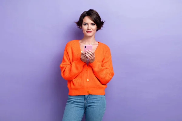 照片上漂亮可爱的女士穿着橙色羊毛衫 传达着现代设备隔离的紫色背景 — 图库照片