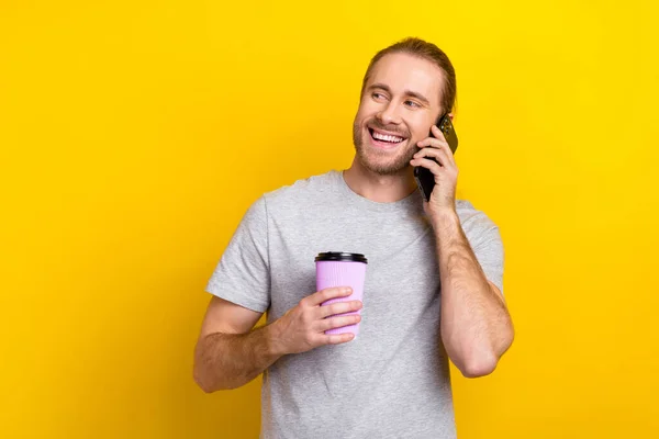 照片中长着长发在电话里交谈的快乐男人拿着一杯咖啡 看起来空荡荡的 被黄色背景隔开了 — 图库照片