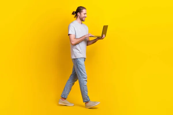 正の満足男の完全な長さの写真は 黄色の色の背景に隔離されたノートパソコン歩く空のスペースを保持ライトシャツジーンズを着用 — ストック写真