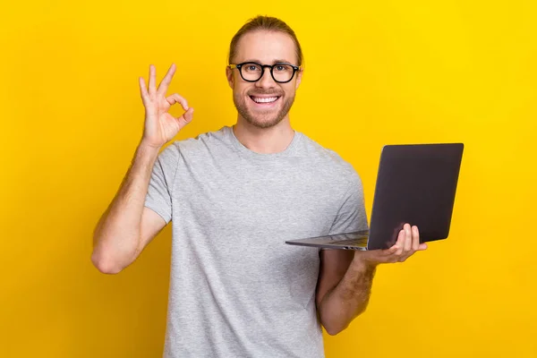 Photo of positive clever man geek wear trendy clothes demonstrate okey symbol quality modern gadget isolated on yellow color background.