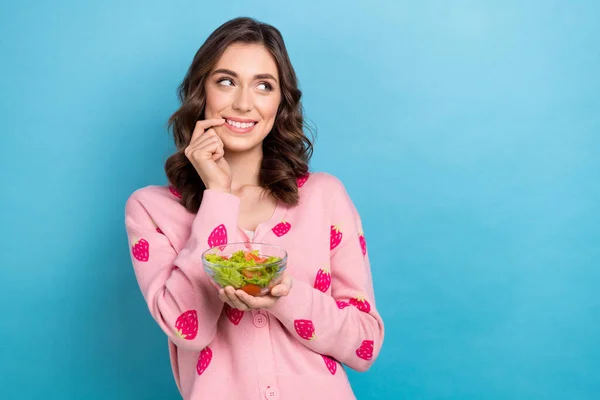 Photo of sweet tricky woman wear pink cardigan looking emtpy space finger lips salad plate isolated blue color background