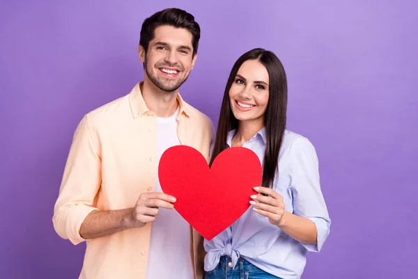 漂亮可爱的夫妻的照片 妻子与丈夫在一起举着红纸大的象征庆祝周年情人节隔离在紫色背景下 — 图库照片