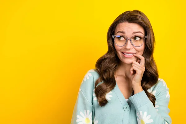 Portrait of young guilty attractive woman curly brown hairstyle bite nail wear glasses look mockup choose advert isolated on yellow color background.