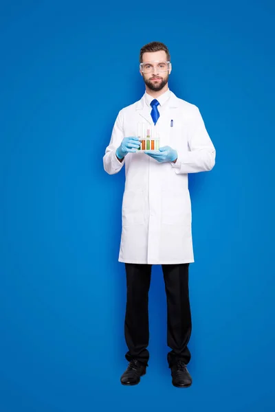 全尺寸 Fullbody 有吸引力的时尚科学家在白色实验室大衣 黑色裤子 蓝色领带持有多色液体的测试管 看着相机 在灰色背景下孤立的肖像 — 图库照片