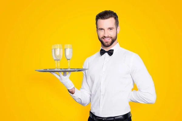 灰色の背景に分離された古典的な白いシャツと黒い弓の後ろやシャンパン スパーク リング ワイン 杯付きのトレイの手を握ってで陽気なフレンドリーな男の肖像 — ストック写真